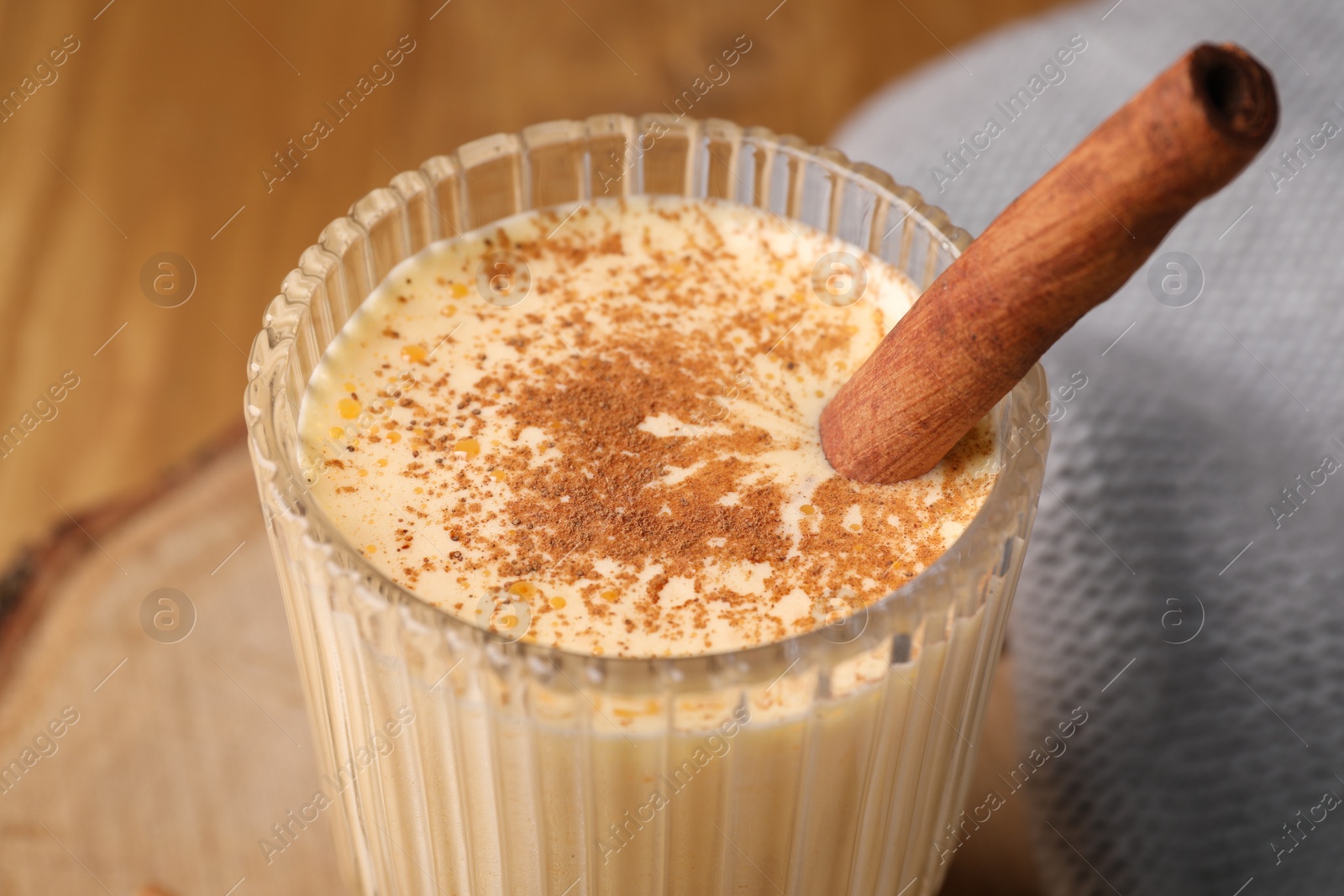 Photo of Glass of delicious eggnog with cinnamon on table, closeup