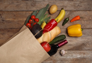 Shopping paper bag with different groceries on wooden background, flat lay