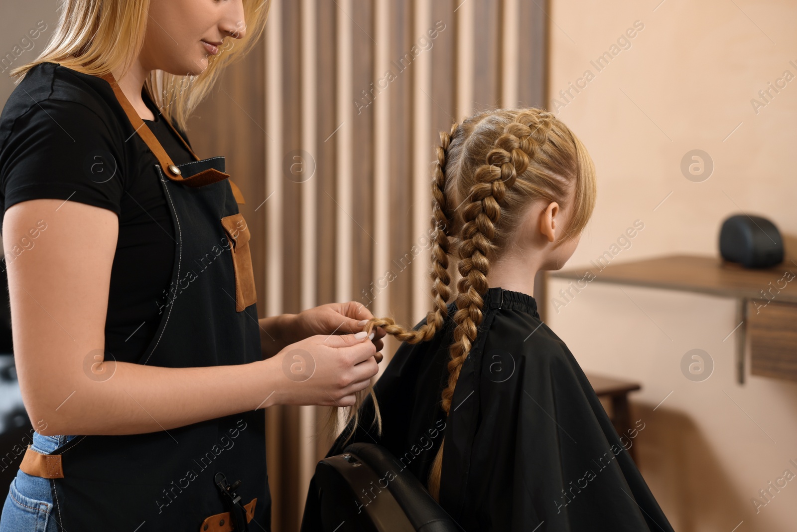 Photo of Professional hairdresser braiding girl's hair in beauty salon, closeup