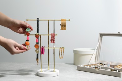 Photo of Woman taking earring from holder with jewelry on light grey table, closeup