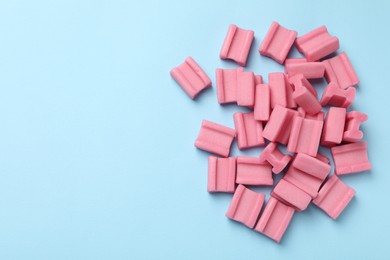 Photo of Tasty pink chewing gums on light blue background, flat lay. Space for text