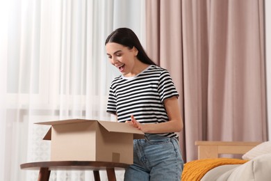 Emotional young woman opening parcel at home. Internet shopping