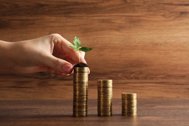 Photo of Woman putting coin onto stack with green sprout at wooden table, closeup. Investment concept