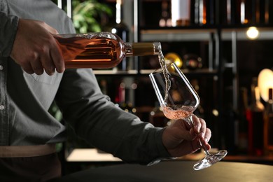 Man pouring rose wine from bottle into glass indoors, closeup