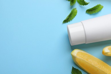 Photo of Blank tube of toothpaste with mint leaves and lemon slices on turquoise background, flat lay. Space for text