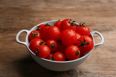 Photo of Fresh ripe cherry tomatoes with water drops in colander on wooden table