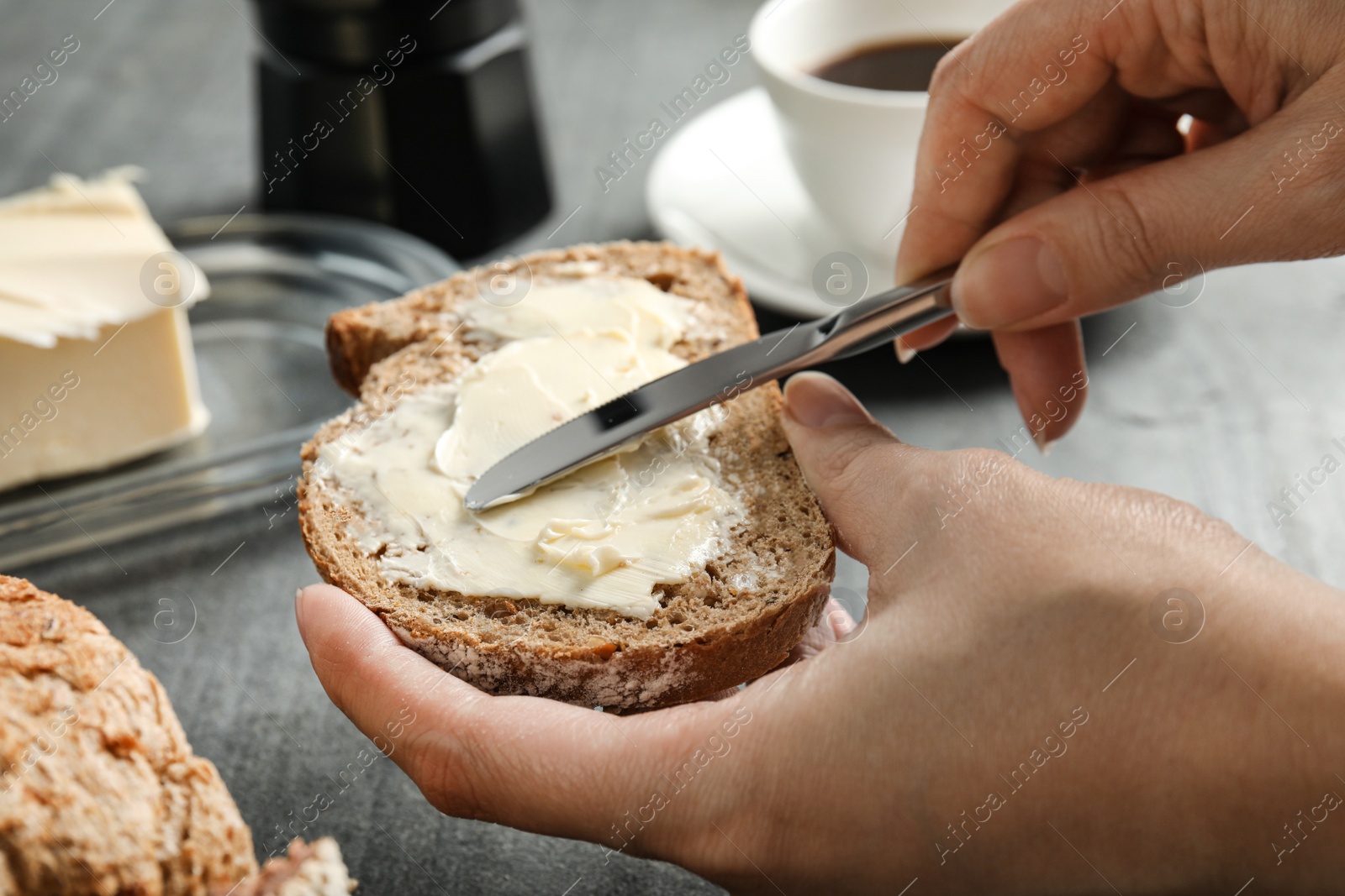 Photo of Woman spreading tasty butter onto bread over grey table, closeup