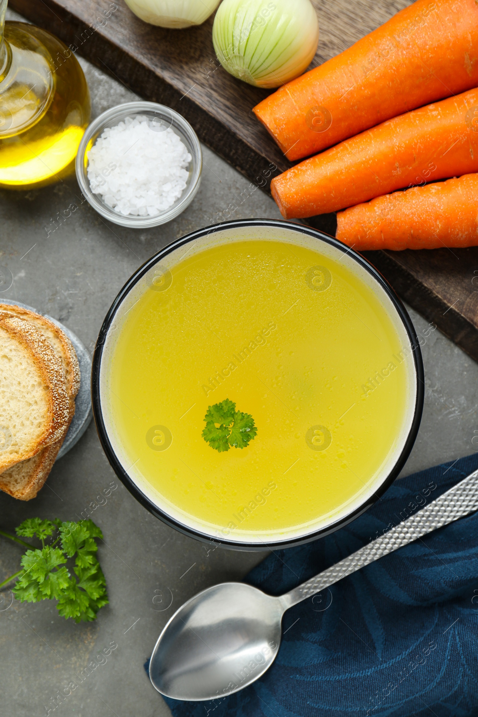 Photo of Delicious chicken bouillon and ingredients on grey table, flat lay