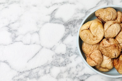 Bowl of dried figs on marble table, top view with space for text. Healthy fruit