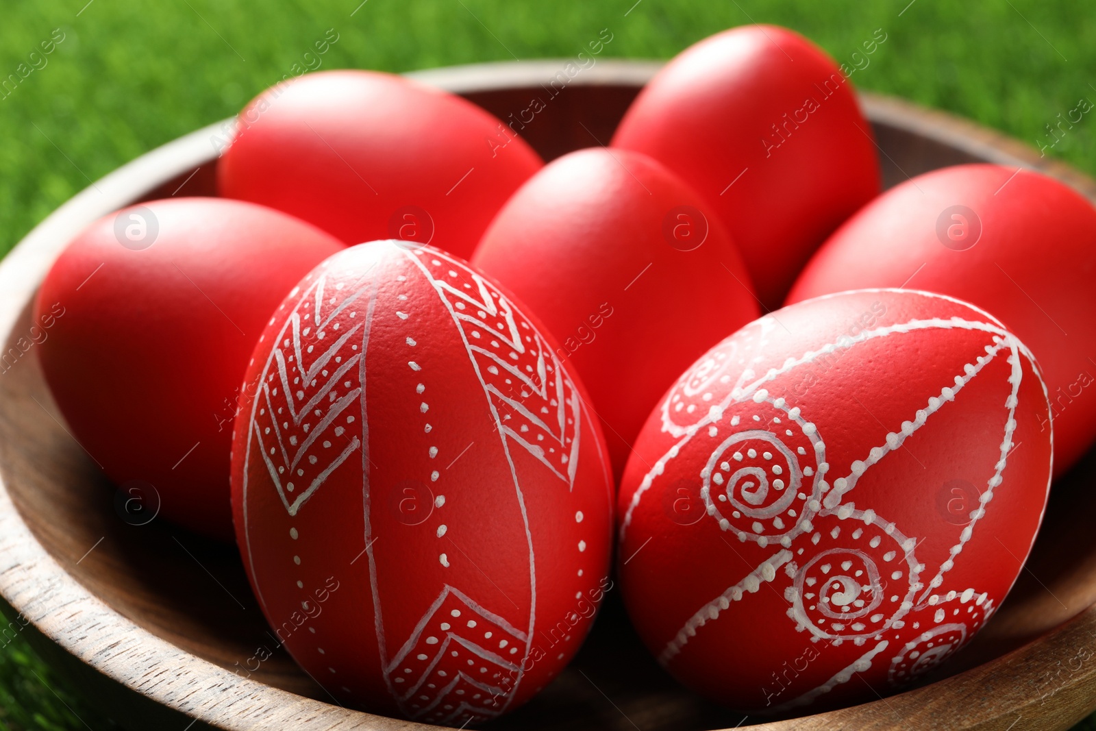 Photo of Wooden bowl with red painted Easter eggs on green grass, closeup