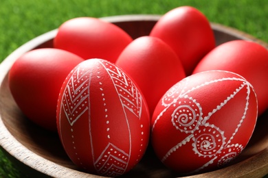 Photo of Wooden bowl with red painted Easter eggs on green grass, closeup