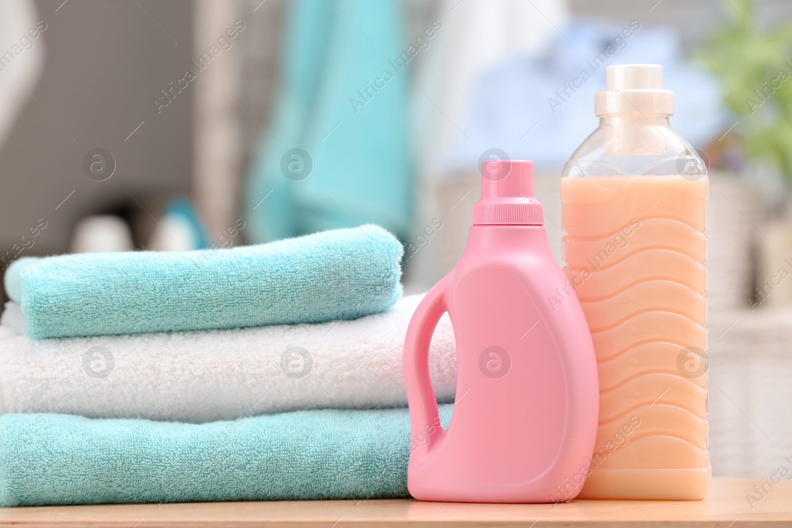 Photo of Stack of clean towels and bottles with detergent on table