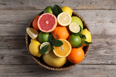 Different fresh citrus fruits and leaves in wicker basket on wooden table, top view