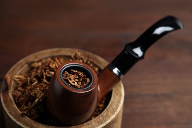 Photo of Smoking pipe and bowl of dry tobacco on table, closeup