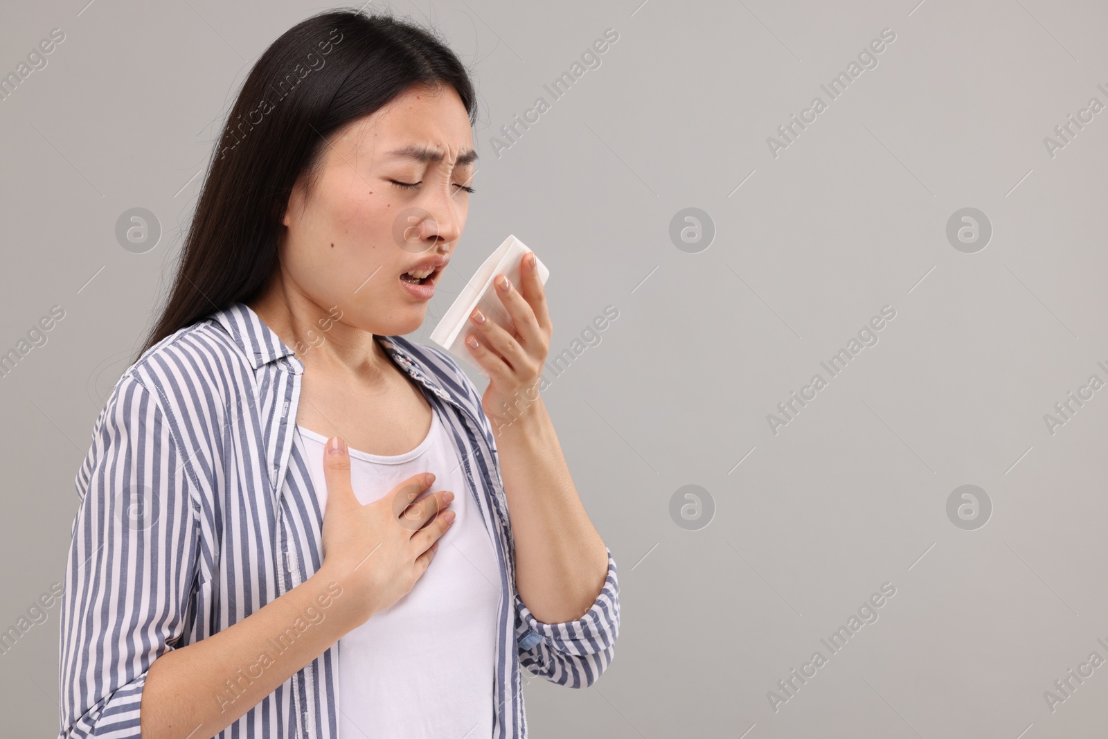 Photo of Suffering from allergy. Young woman with tissue sneezing on grey background, space for text