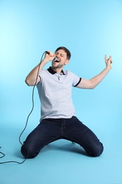 Photo of Handsome man in casual clothes singing with microphone on color background