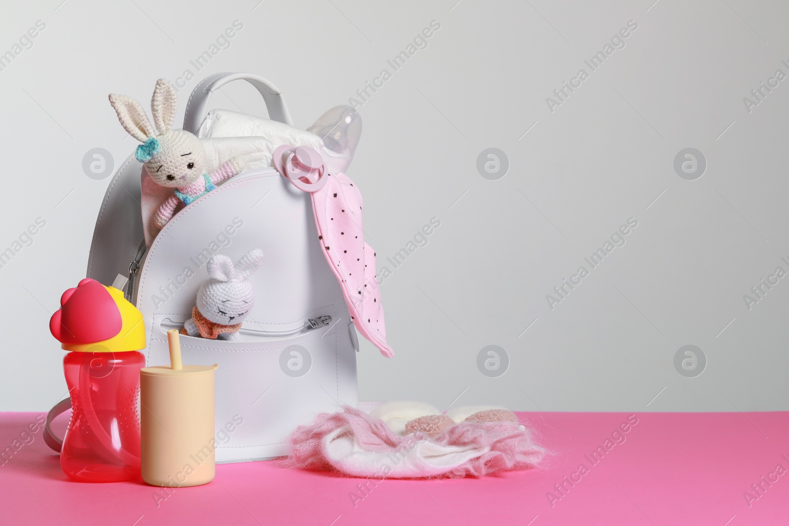 Photo of Mother's backpack with baby's stuff on pink surface against grey background. Space for text