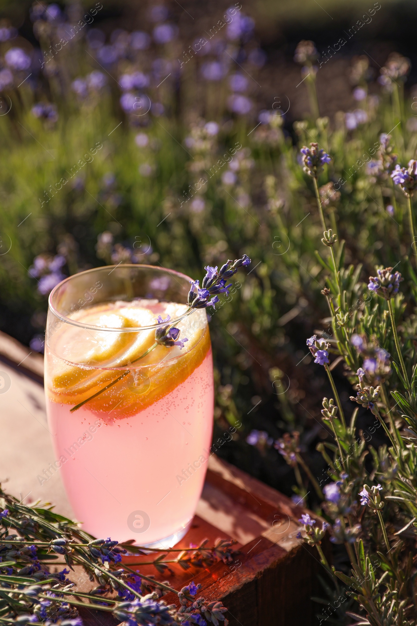 Photo of Glass of fresh lemonade on wooden tray in lavender field