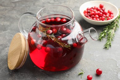 Photo of Tasty hot cranberry tea in teapot, rosemary and fresh berries on light grey textured table