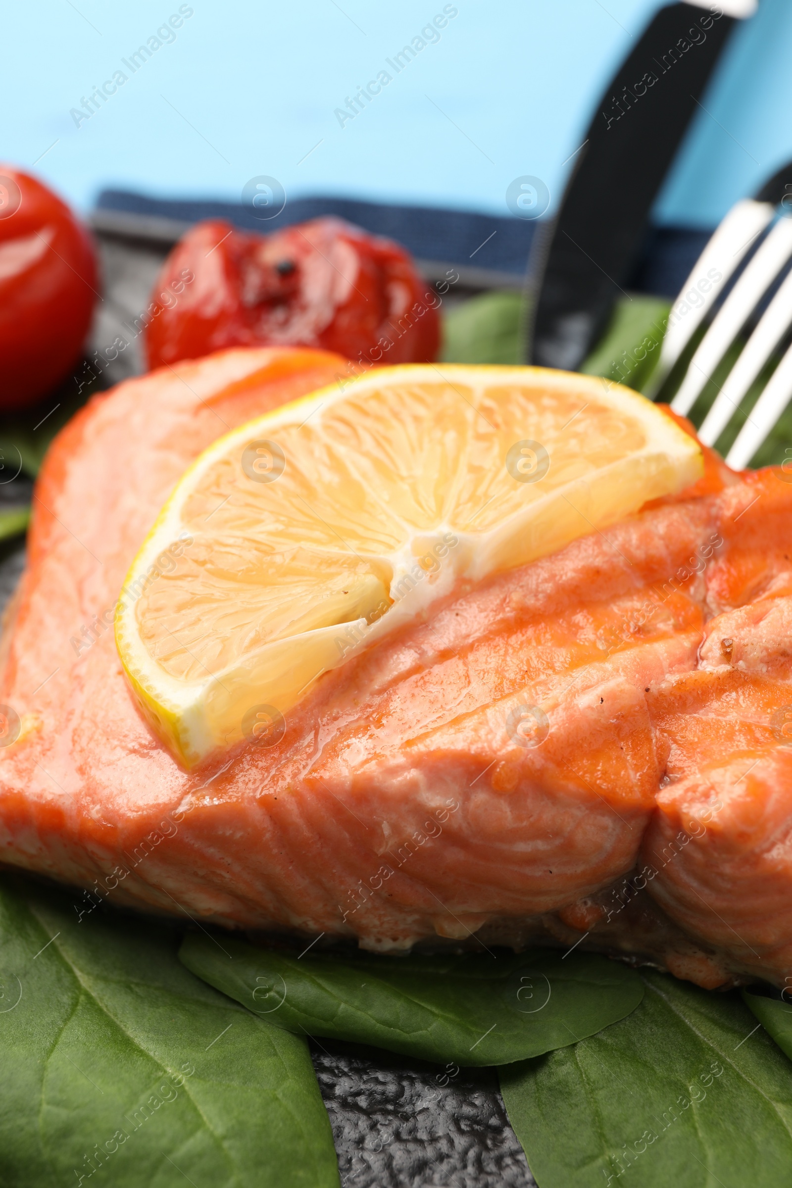 Photo of Tasty grilled salmon with tomatoes, spinach and lemon on table, closeup