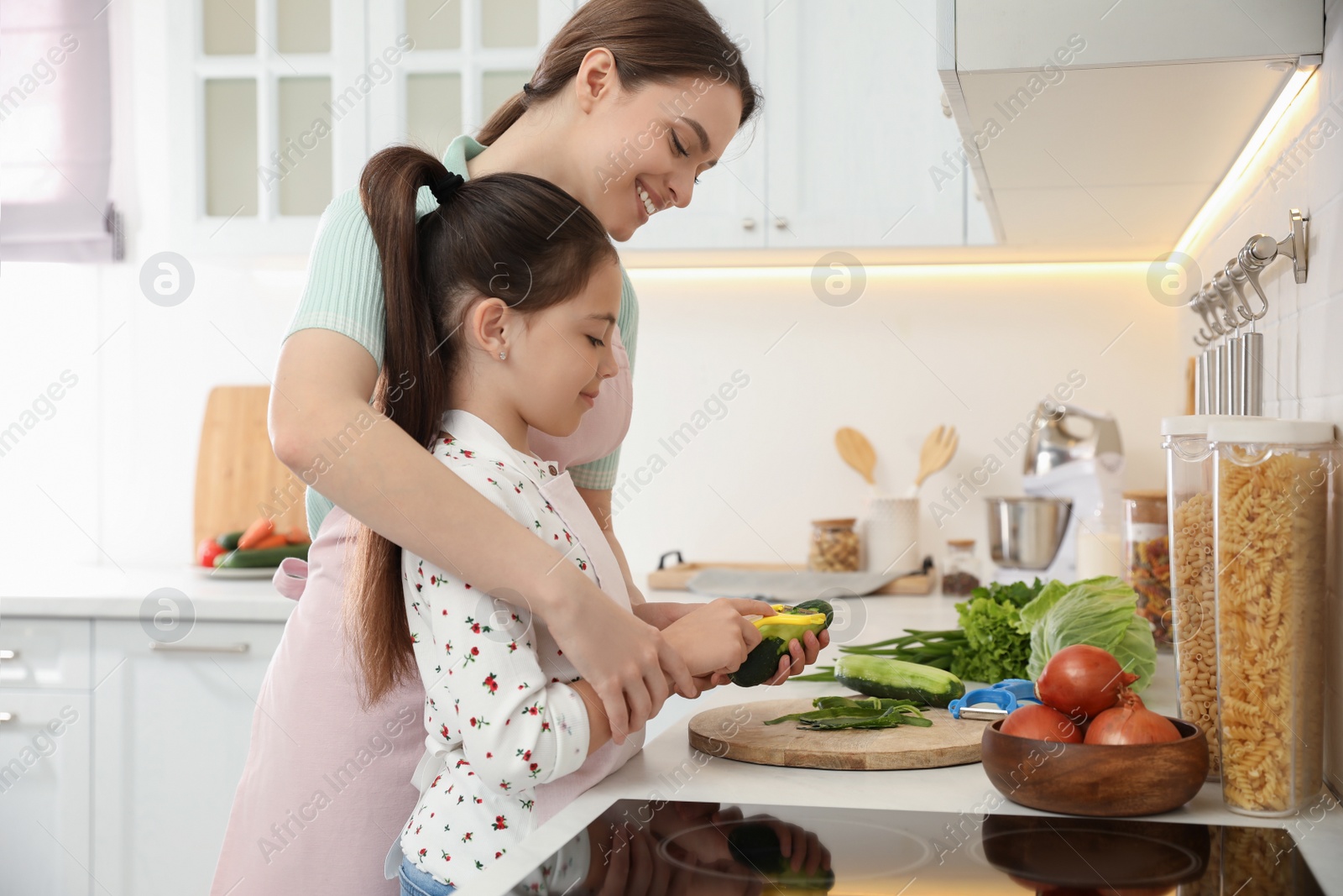 Photo of Mother teaching daughter to peel vegetable at kitchen counter