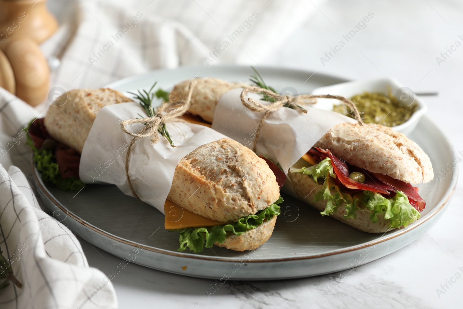 Photo of Delicious sandwiches with bresaola, lettuce and cheese on white marble table, closeup