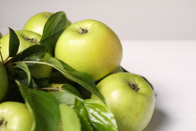 Photo of Fresh ripe green apples with leaves on white table, closeup. Space for text