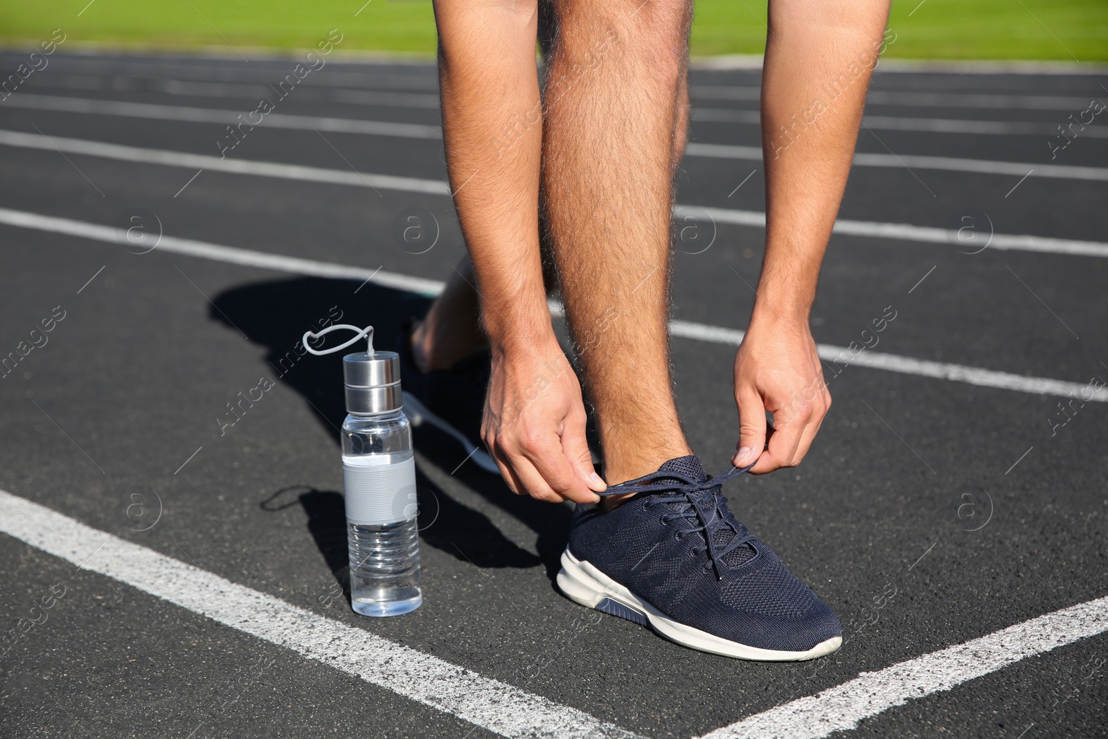 Photo of Sporty man tying shoelaces before running at stadium on sunny morning