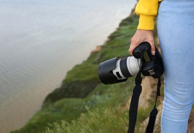 Female photographer with professional camera outdoors, closeup. Space for text