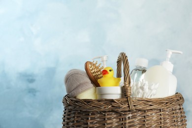 Photo of Wicker basket full of different baby cosmetic products, accessories and toy on light blue background, closeup. Space for text