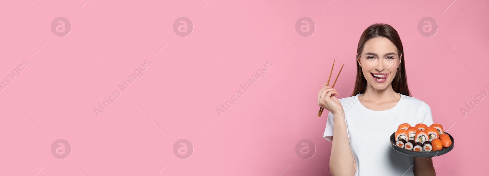 Photo of Happy young woman with plate of sushi rolls and chopsticks on pink background. Space for text