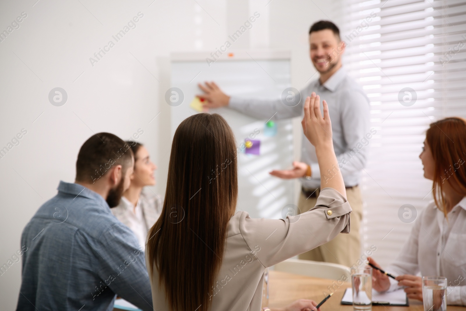 Photo of Young woman raising hand to ask question at business training in conference room