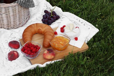 Photo of Picnic blanket with tasty food and basket on green grass outdoors