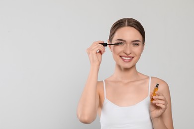 Young woman applying oil onto her eyelashes on white background, space for text