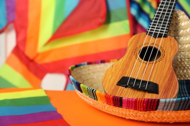Mexican sombrero hat and ukulele on orange table, closeup. Space for text