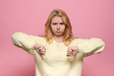 Photo of Dissatisfied young woman showing thumbs down on pink background