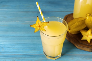 Photo of Delicious carambola juice and fresh fruits on light blue wooden table. Space for text