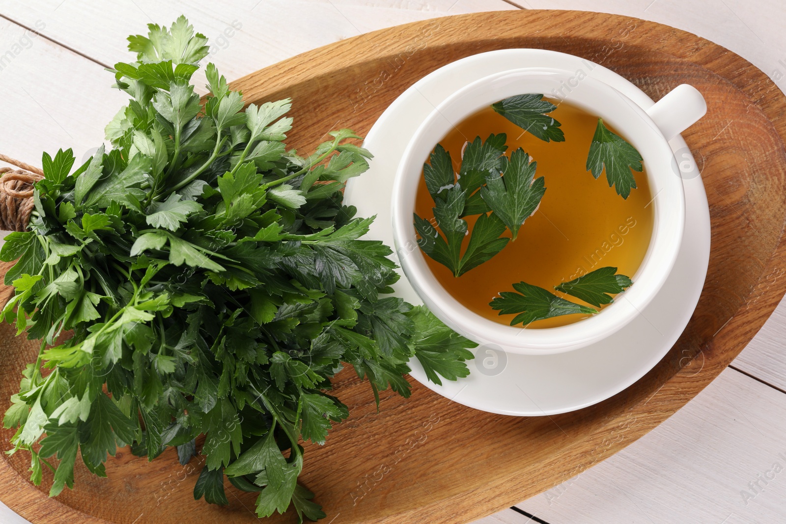 Photo of Aromatic herbal tea and fresh parsley on white wooden table, top view