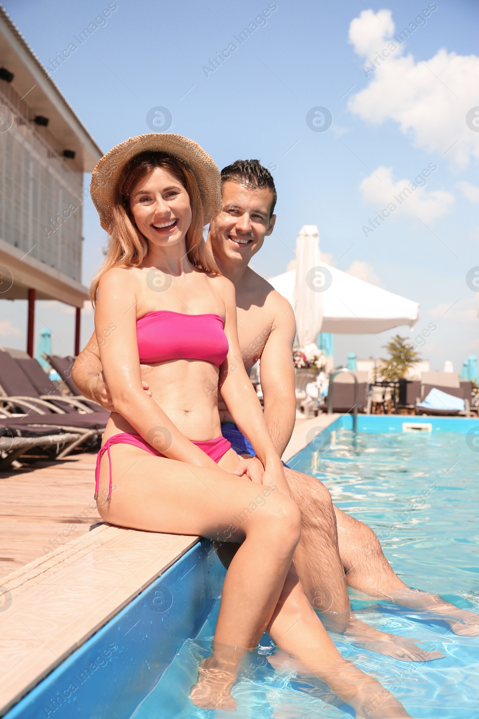 Photo of Happy couple sitting near blue swimming pool outdoors