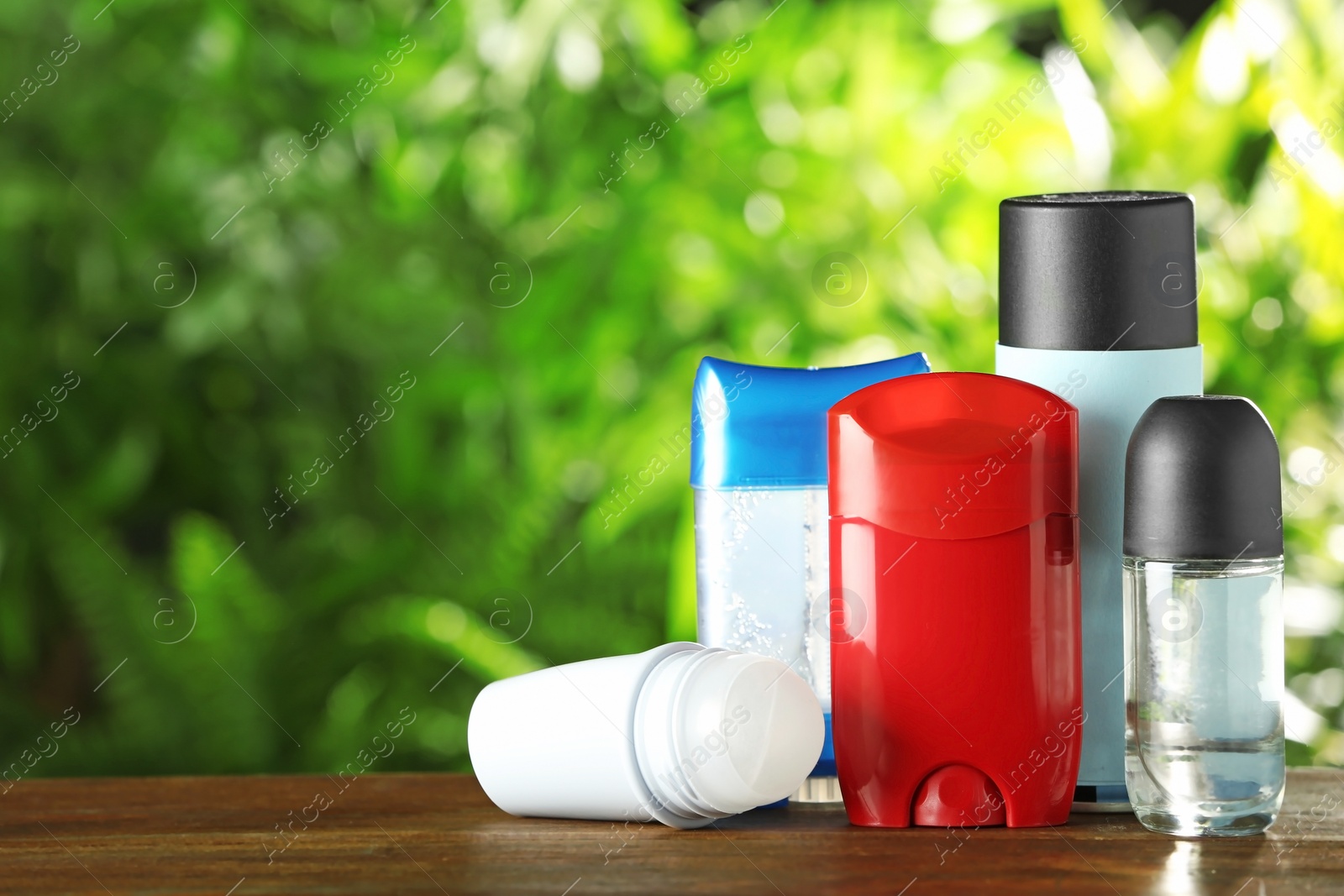 Photo of Set of different deodorants on wooden table against blurred green background. Space for text