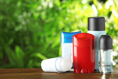 Photo of Set of different deodorants on wooden table against blurred green background. Space for text