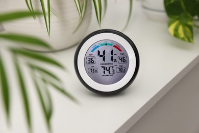 Photo of Digital hygrometer with thermometer and plants on white table