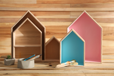 Painted house shaped shelves, brushes and plant on wooden table. Interior elements