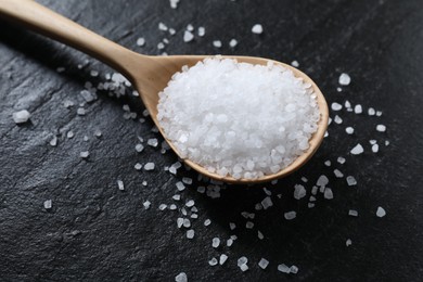 Photo of Organic white salt and spoon on black table, closeup