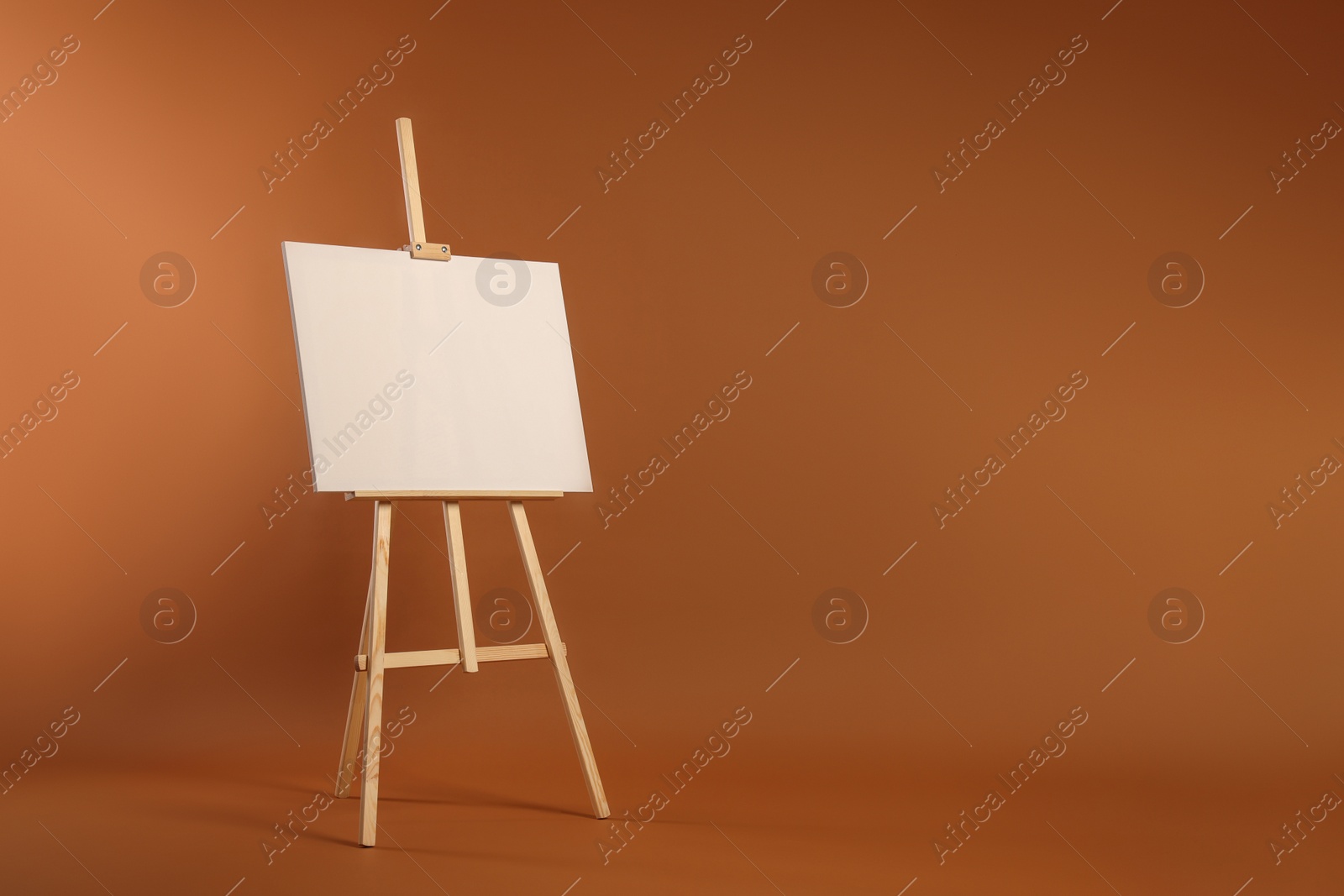 Photo of Wooden easel with blank canvas on brown background. Space for text