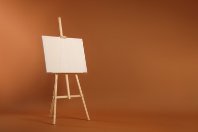 Photo of Wooden easel with blank canvas on brown background. Space for text