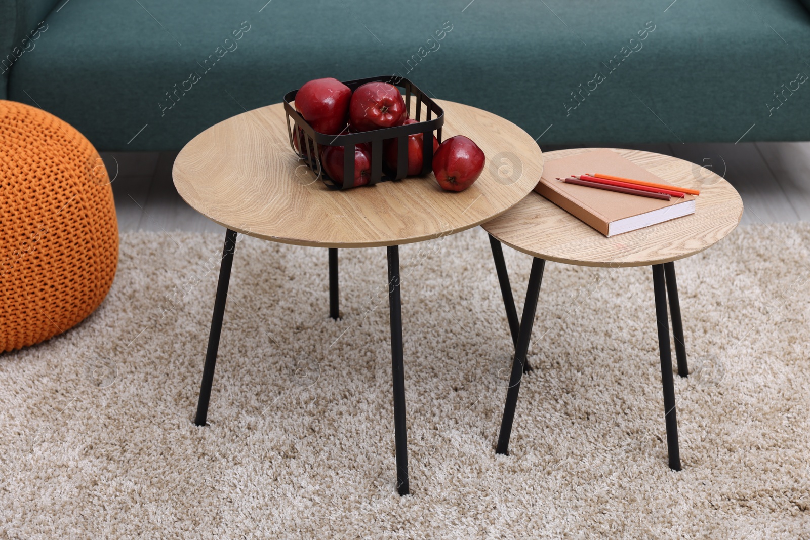 Photo of Red apples, book and pencils on nesting tables indoors