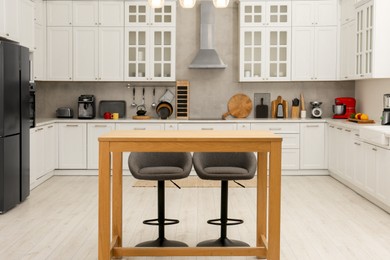 Photo of Stylish modern furniture and wooden table with bar chairs in kitchen. Interior design