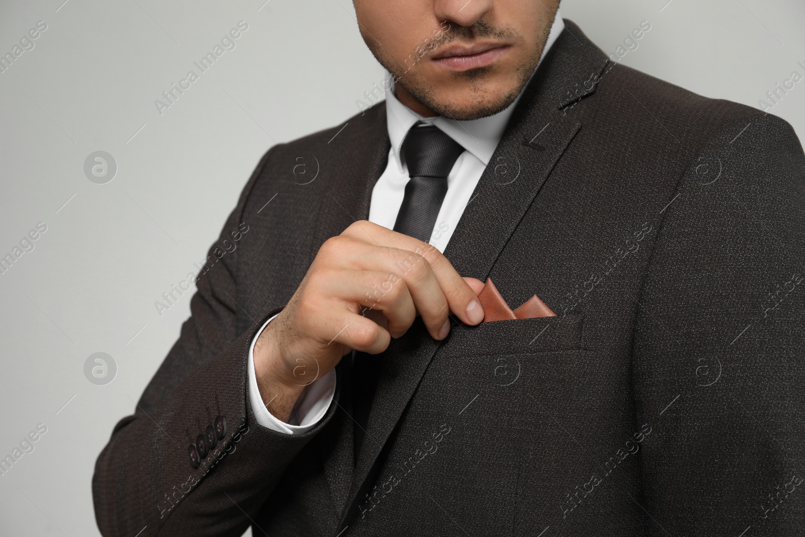 Photo of Man fixing handkerchief in breast pocket of his suit on light background, closeup