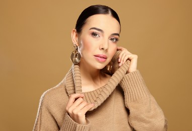 Photo of Beautiful young woman with elegant earrings on light brown background